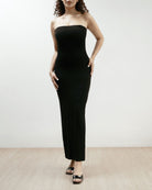 Woman wearing a black strapless dress on a plain background.