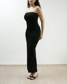 Woman wearing a black strapless dress on a plain background.