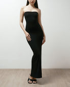 Woman wearing a black strapless dress on a plain background.