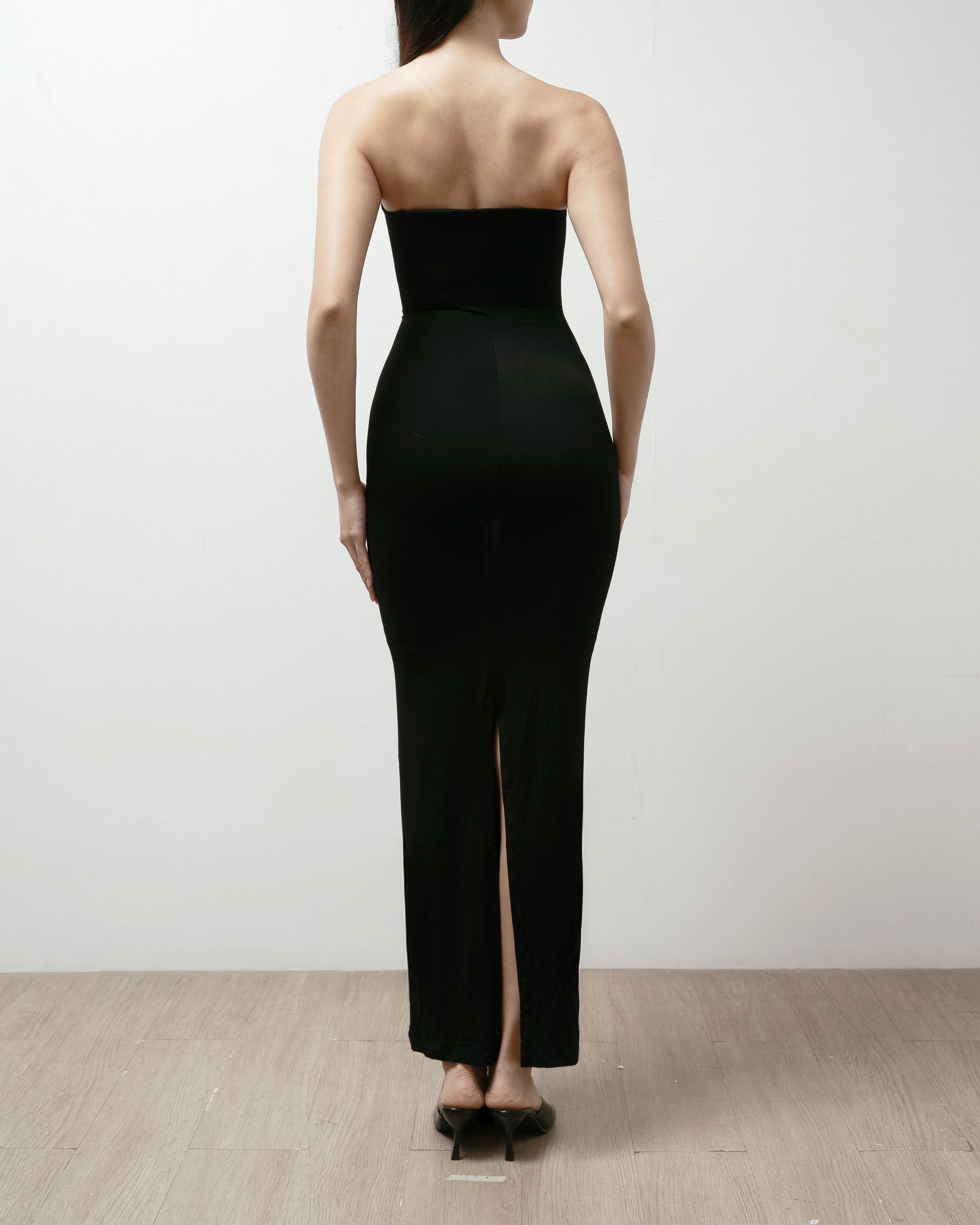 Woman wearing a black strapless dress on a plain background.