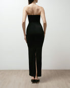 Woman wearing a black strapless dress on a plain background.