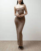 Woman wearing a brown strapless dress on a plain background.