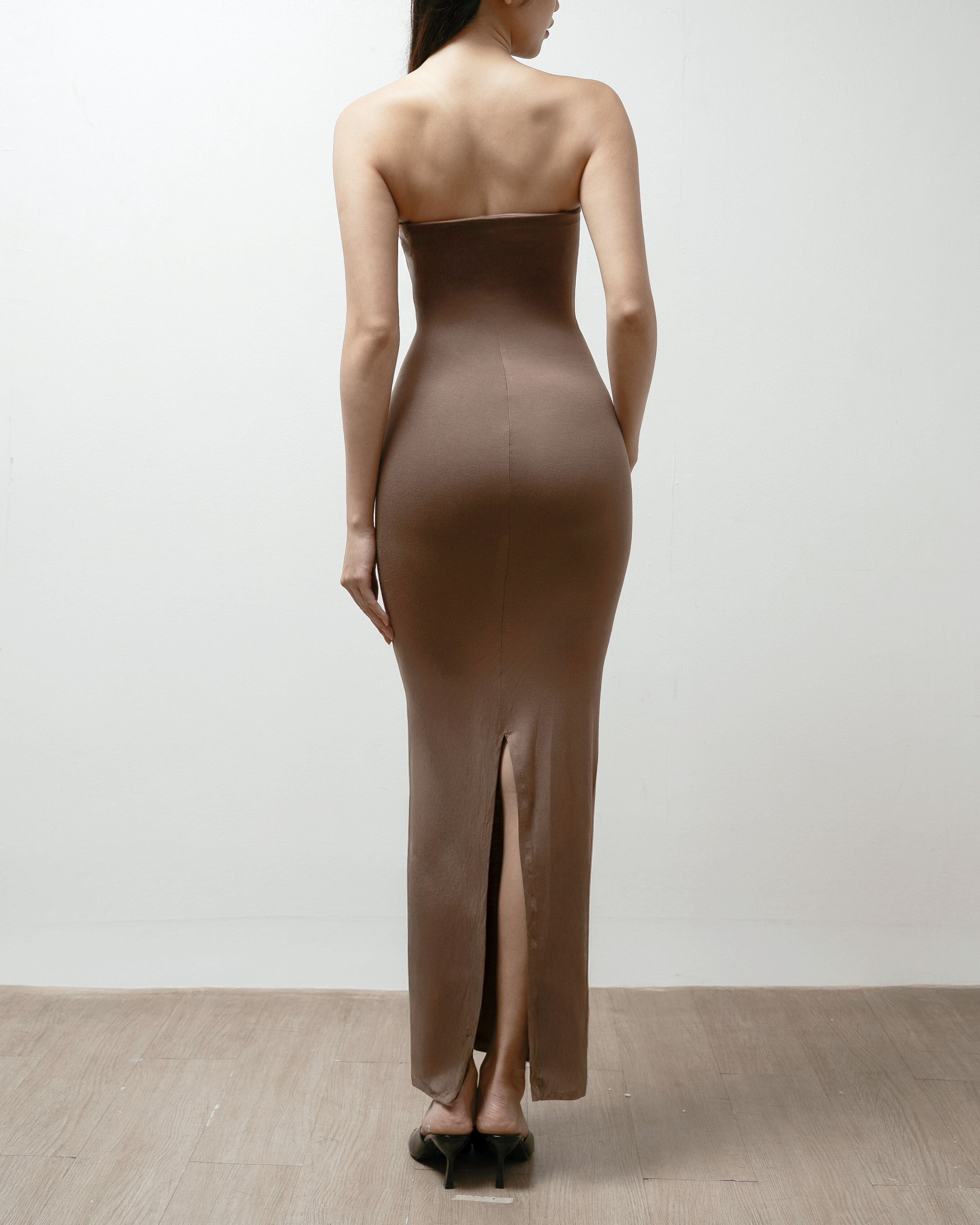 Woman wearing a brown strapless dress on a plain background.