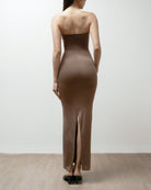 Woman wearing a brown strapless dress on a plain background.