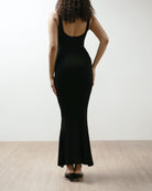 Person wearing a black dress standing against a white wall.