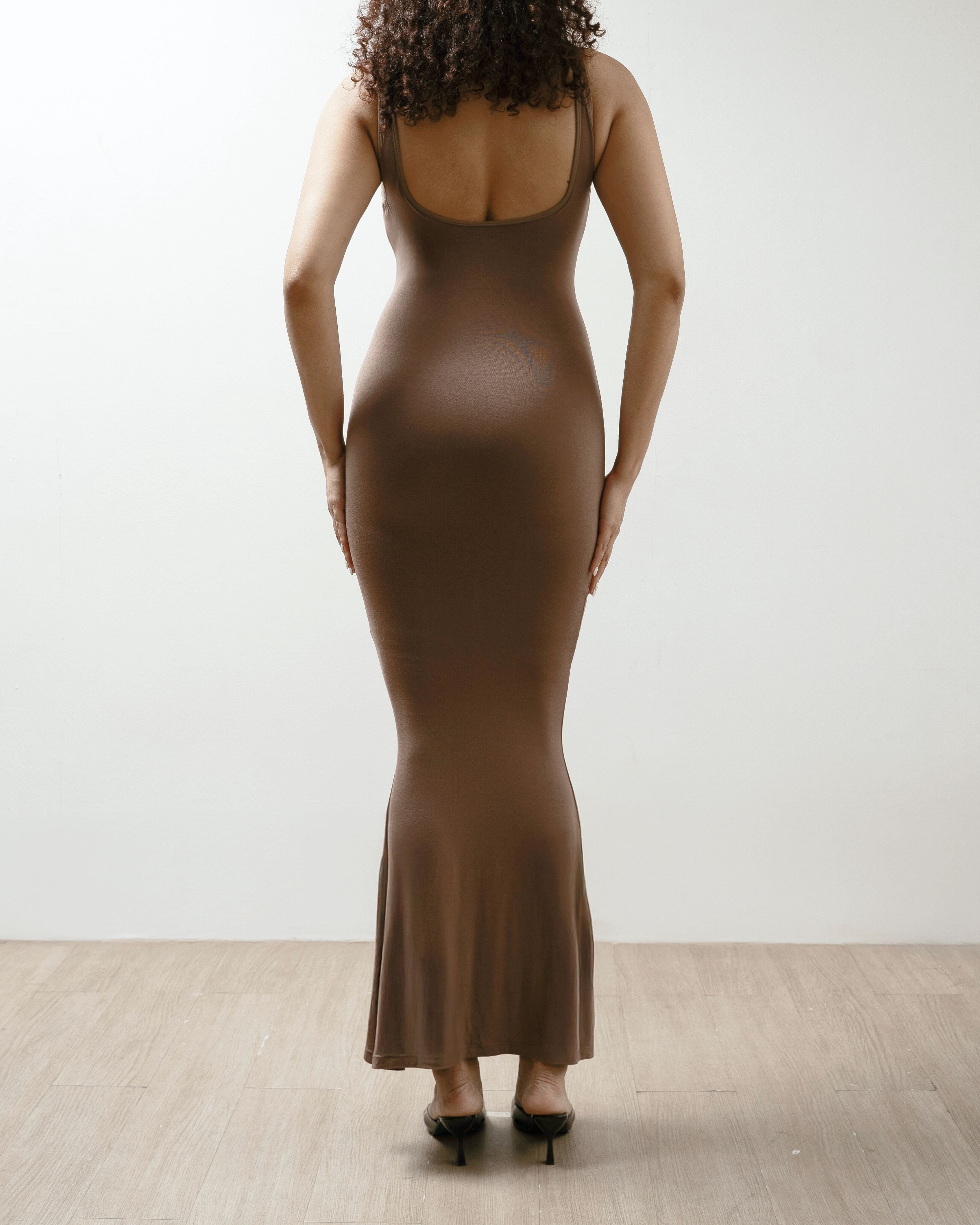 Woman wearing a brown dress against a white wall.