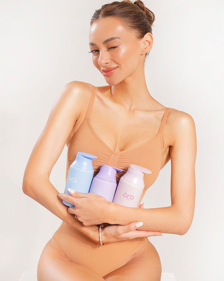A woman wearing a shapewear holding a three lotion bottles
