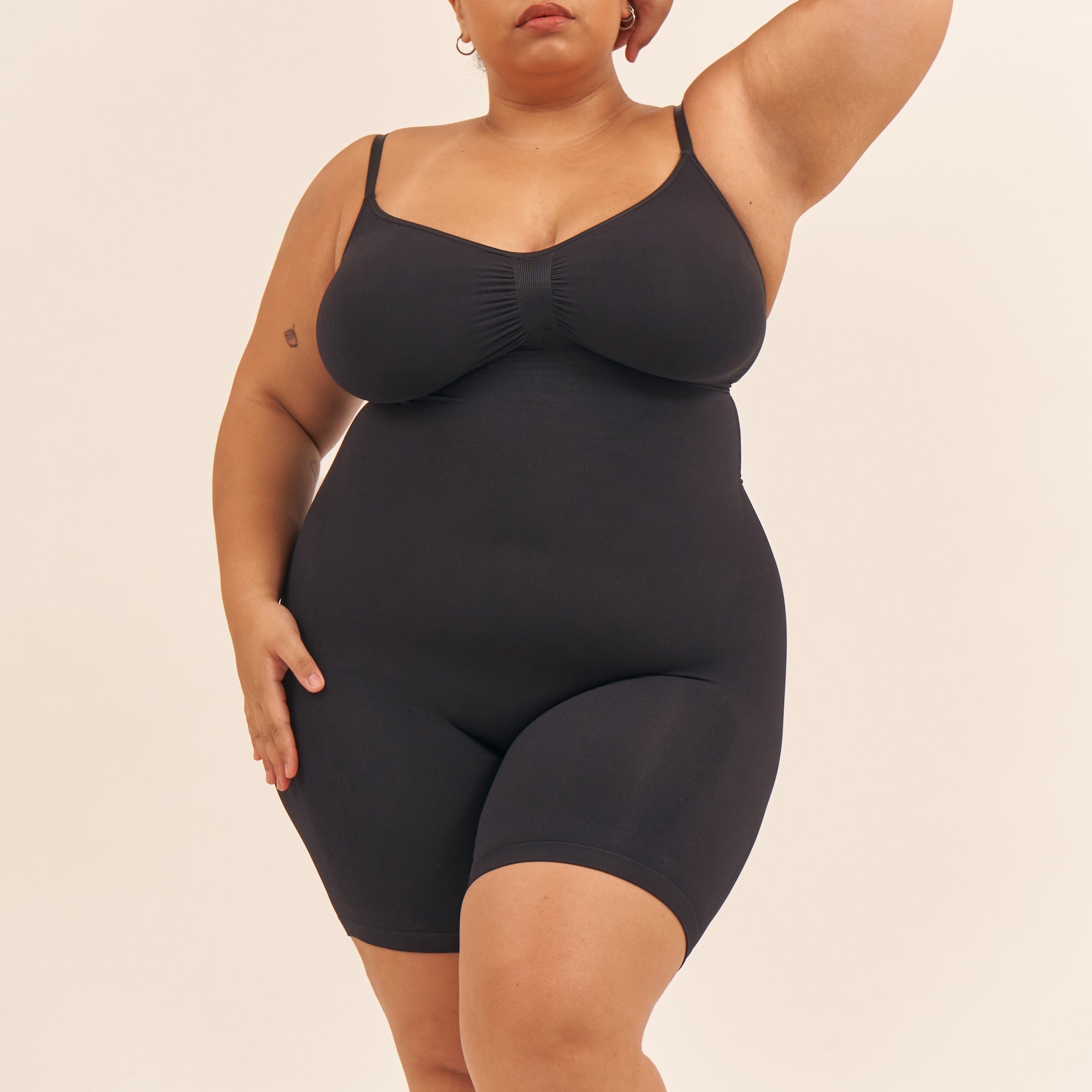 Person wearing a black bodysuit against a beige background