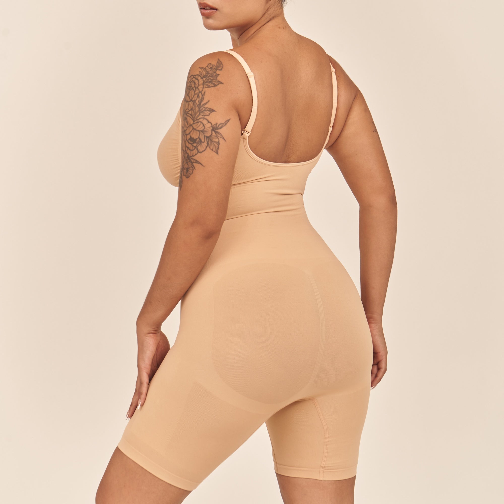 Person wearing a beige bodysuit against a beige background