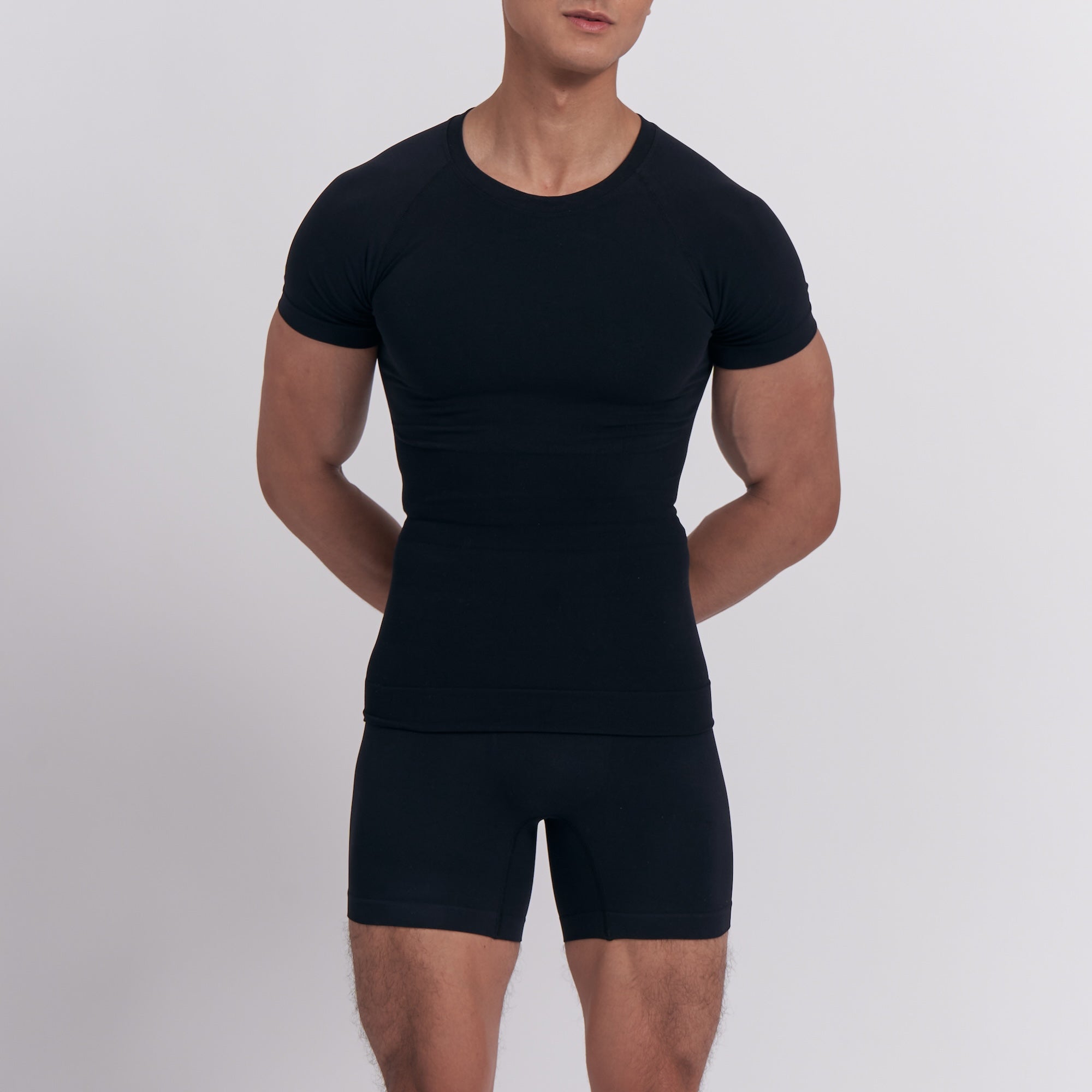 Person wearing a black compression shirt and shorts set on a light gray background