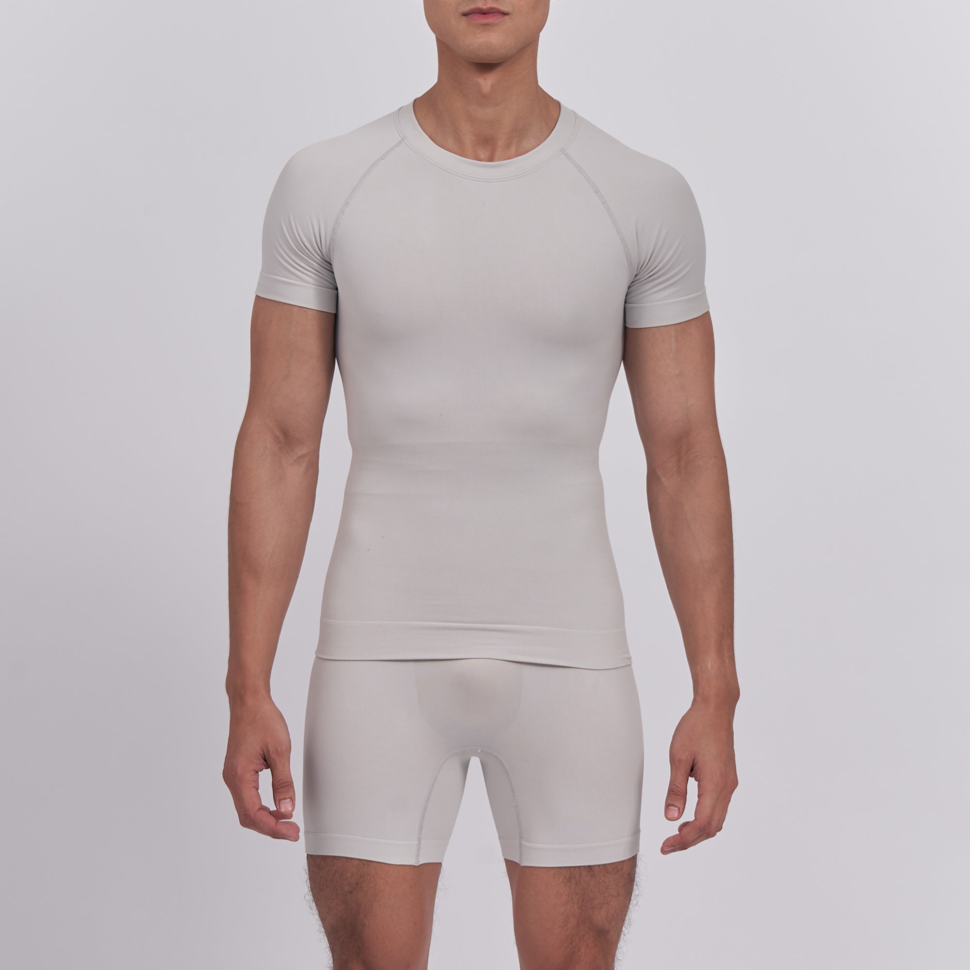 Man wearing a beige compression shirt and shorts set on a light gray background