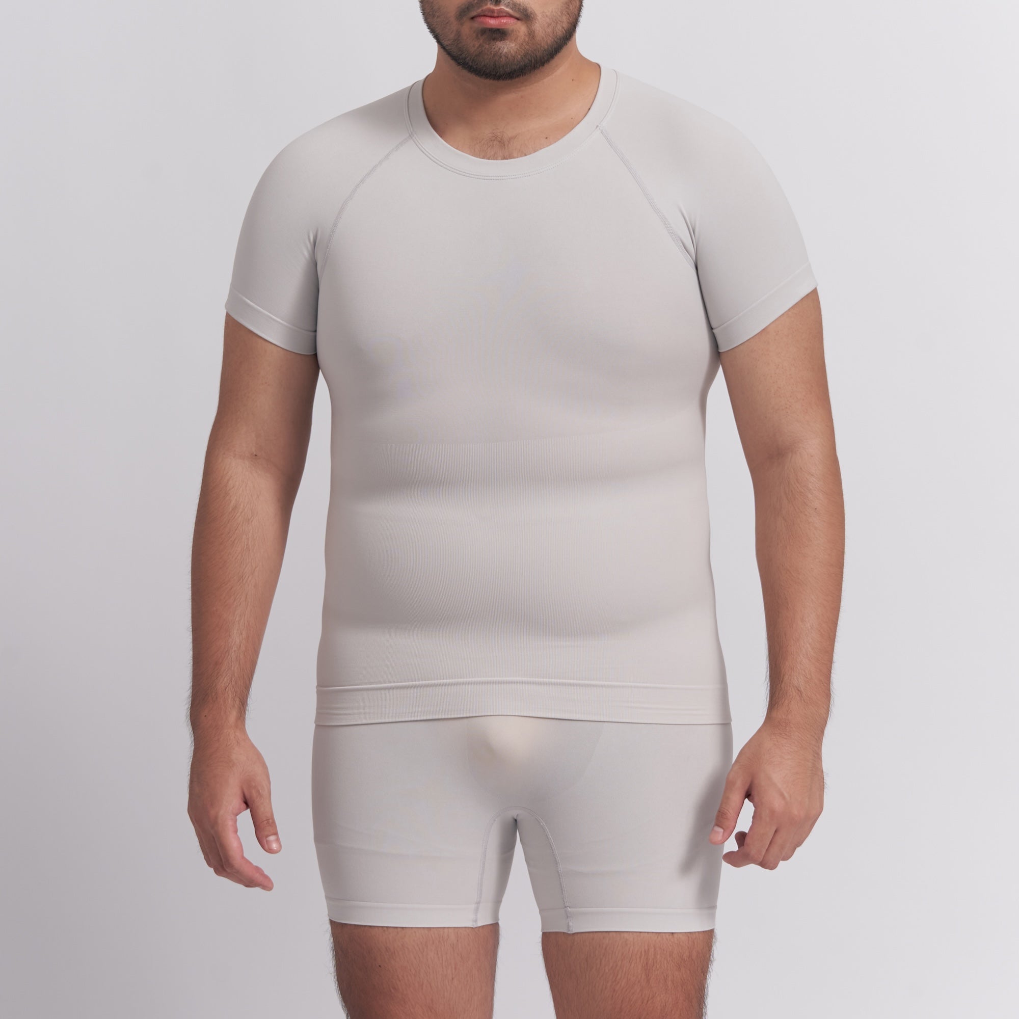 Man wearing a beige compression shirt and shorts set on a light gray background
