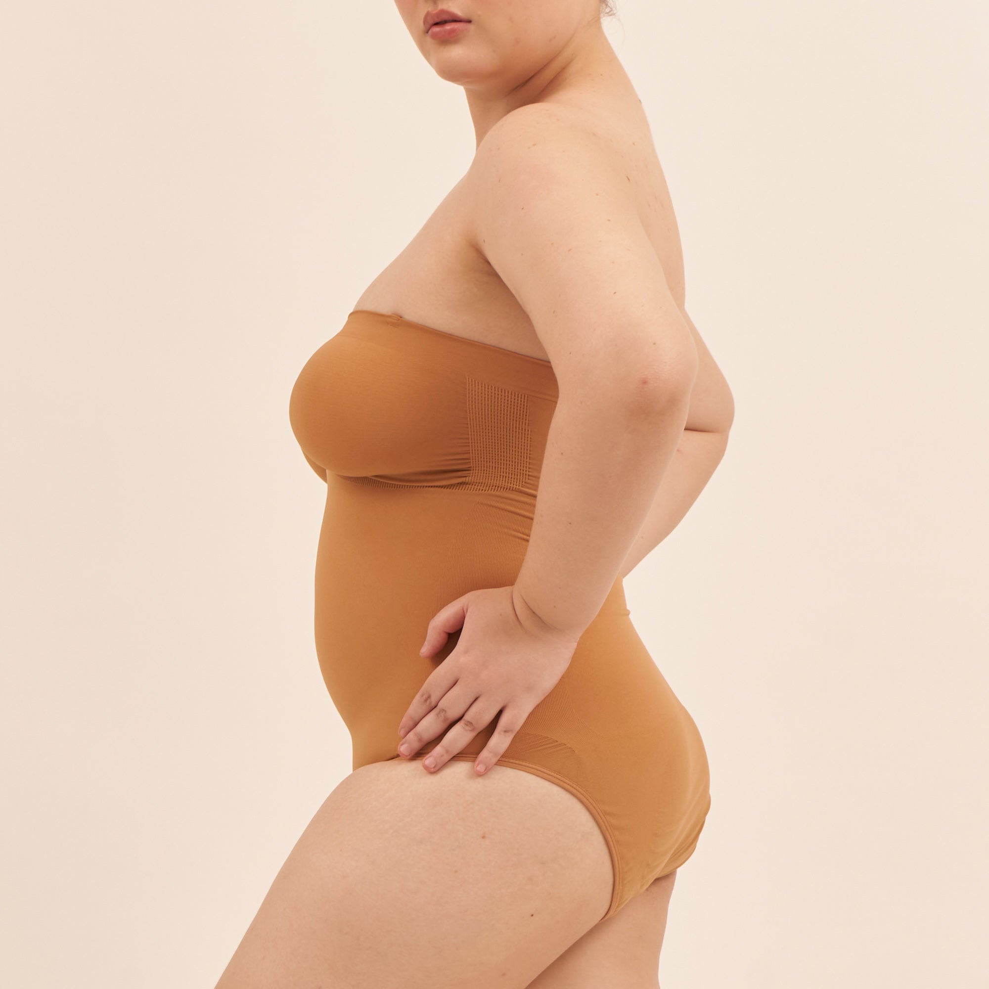 Person wearing a strapless brown bodysuit against a beige background