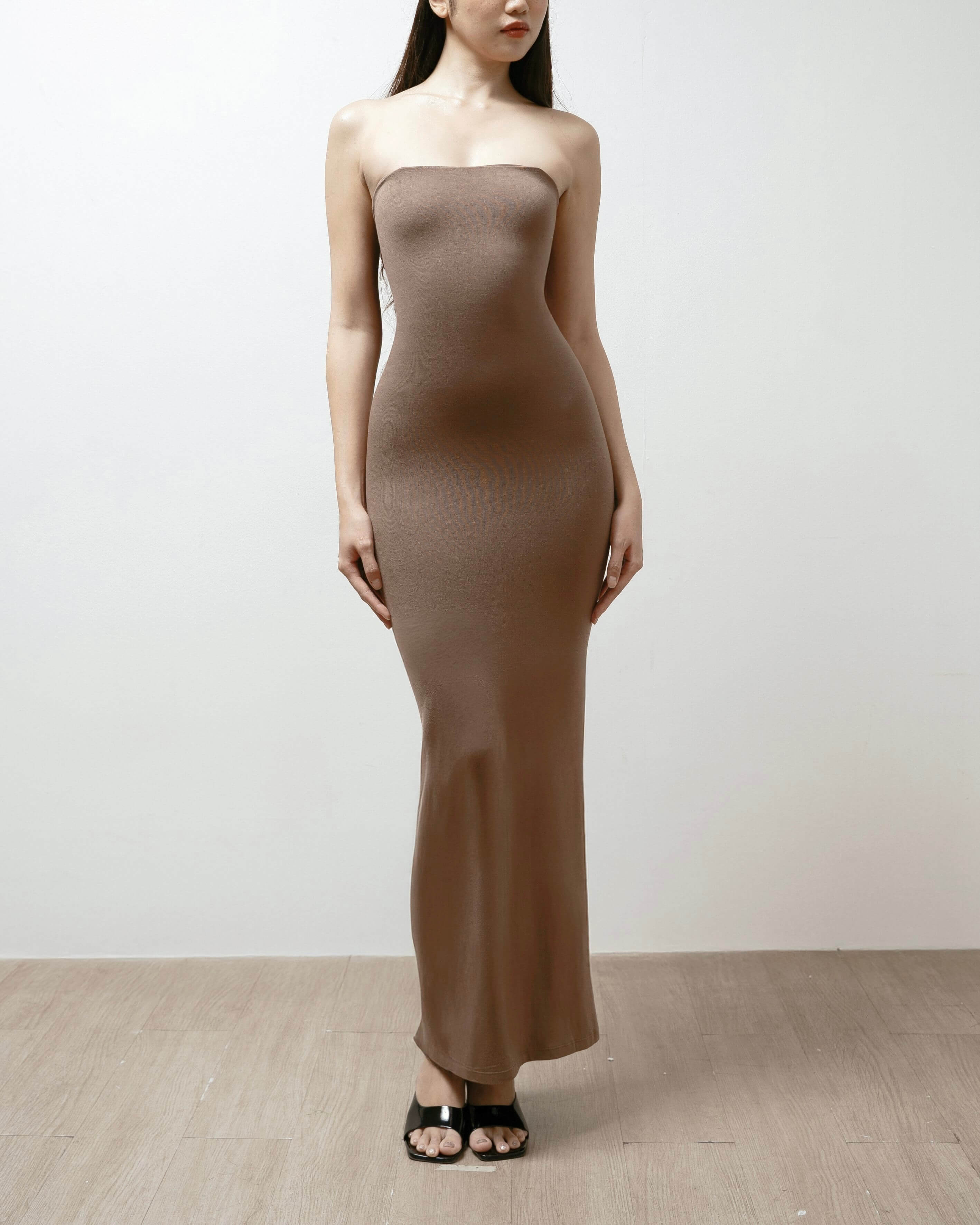 Woman wearing a strapless brown dress against a white background.