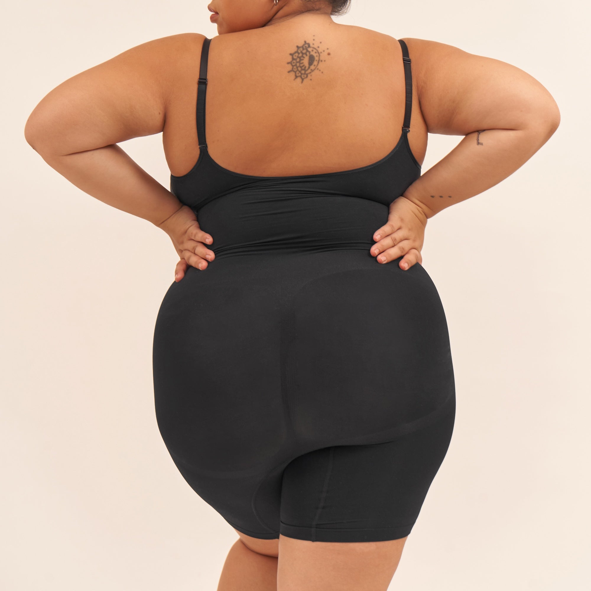 Person wearing a black shapewear garment on a beige background