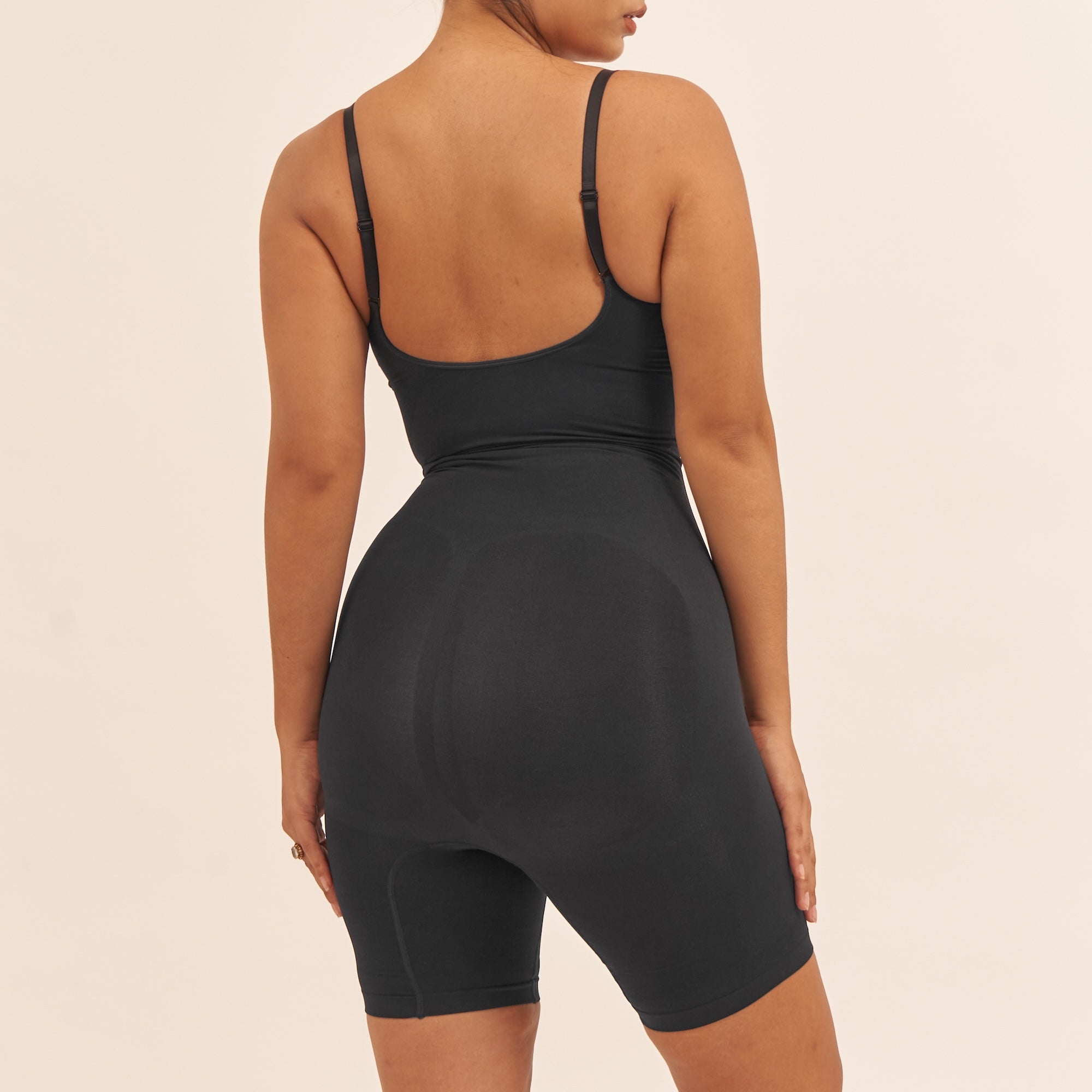Person wearing a black tank top and shorts set on a beige background