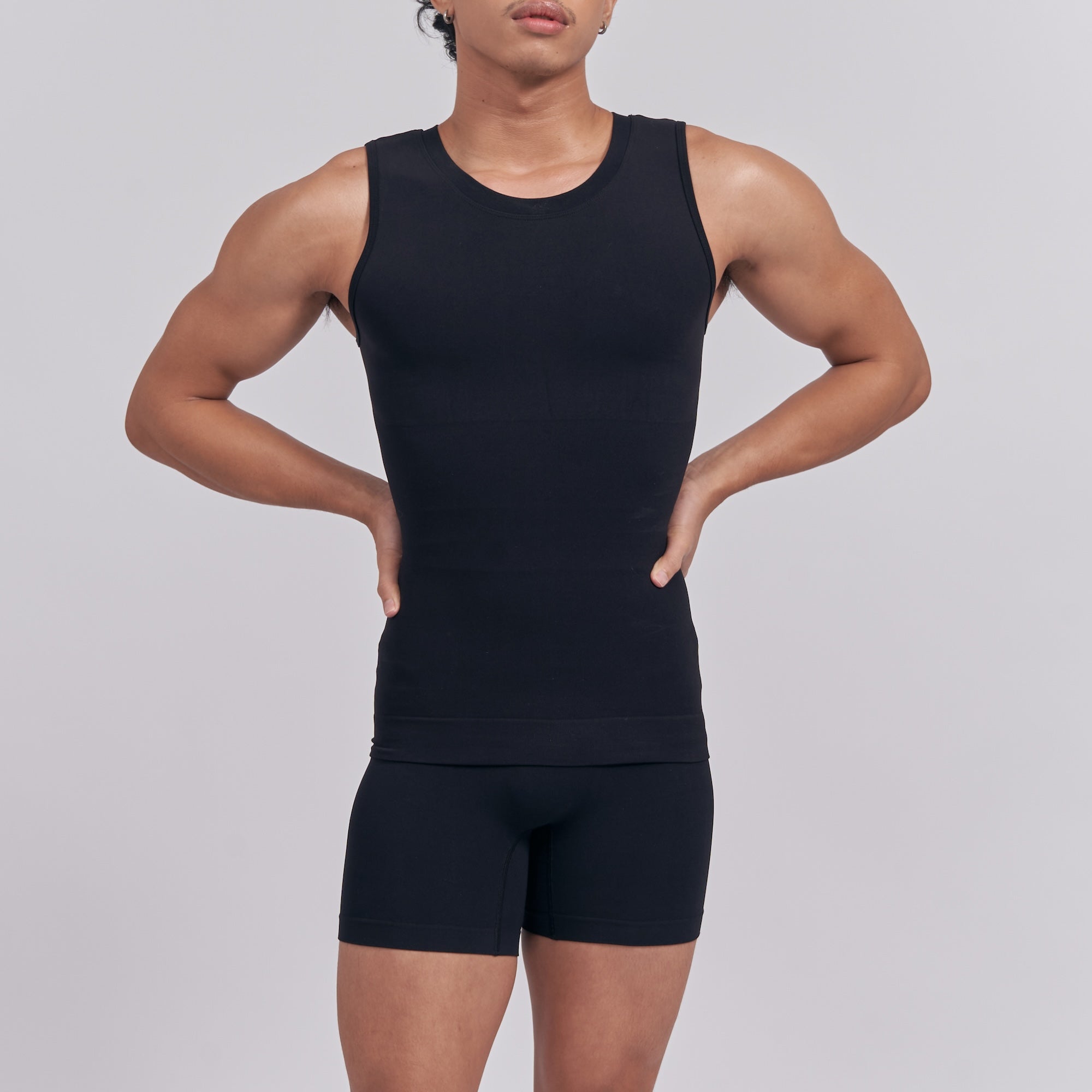 Person wearing a black tank top and shorts on a gray background