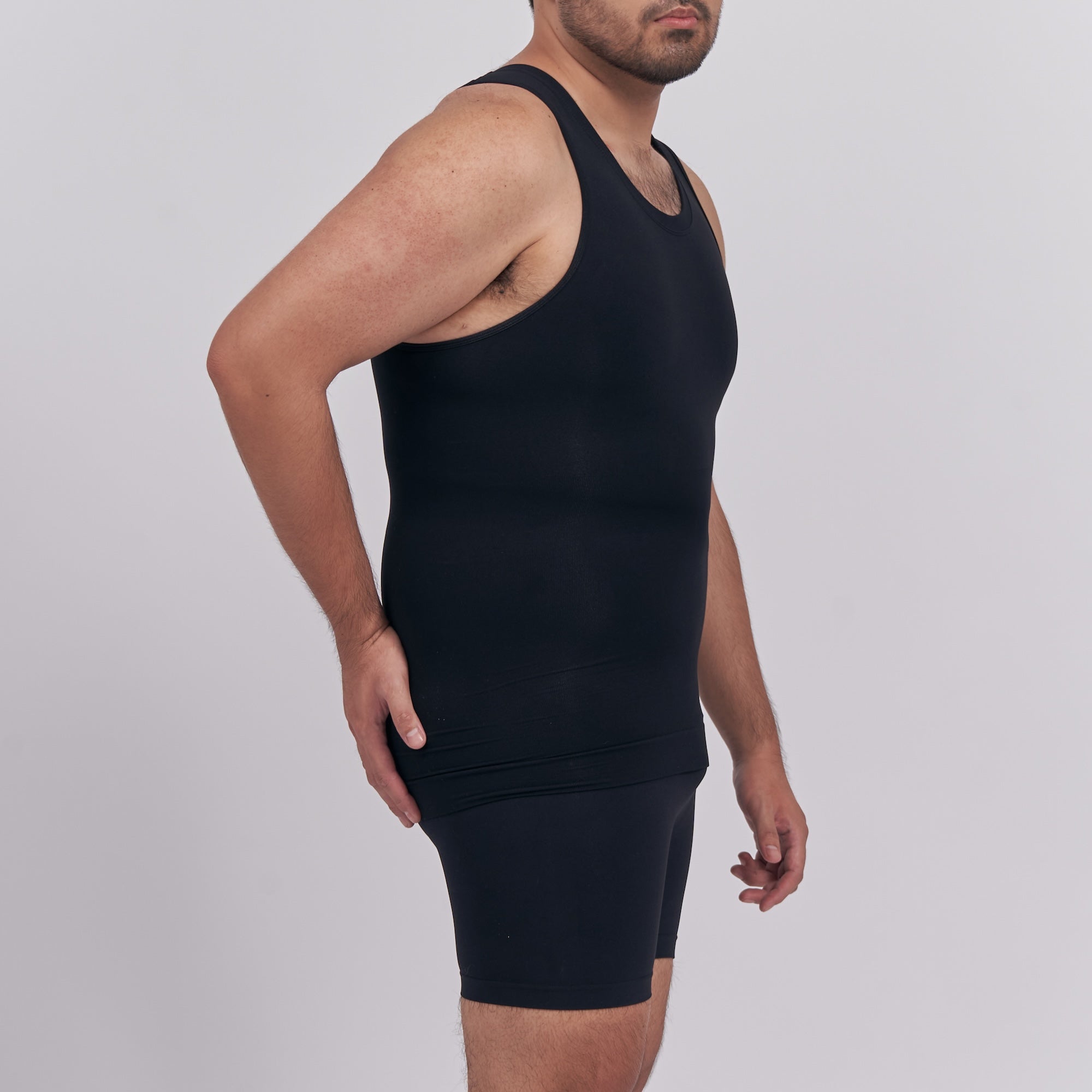 Person wearing a black tank top and shorts on a light gray background