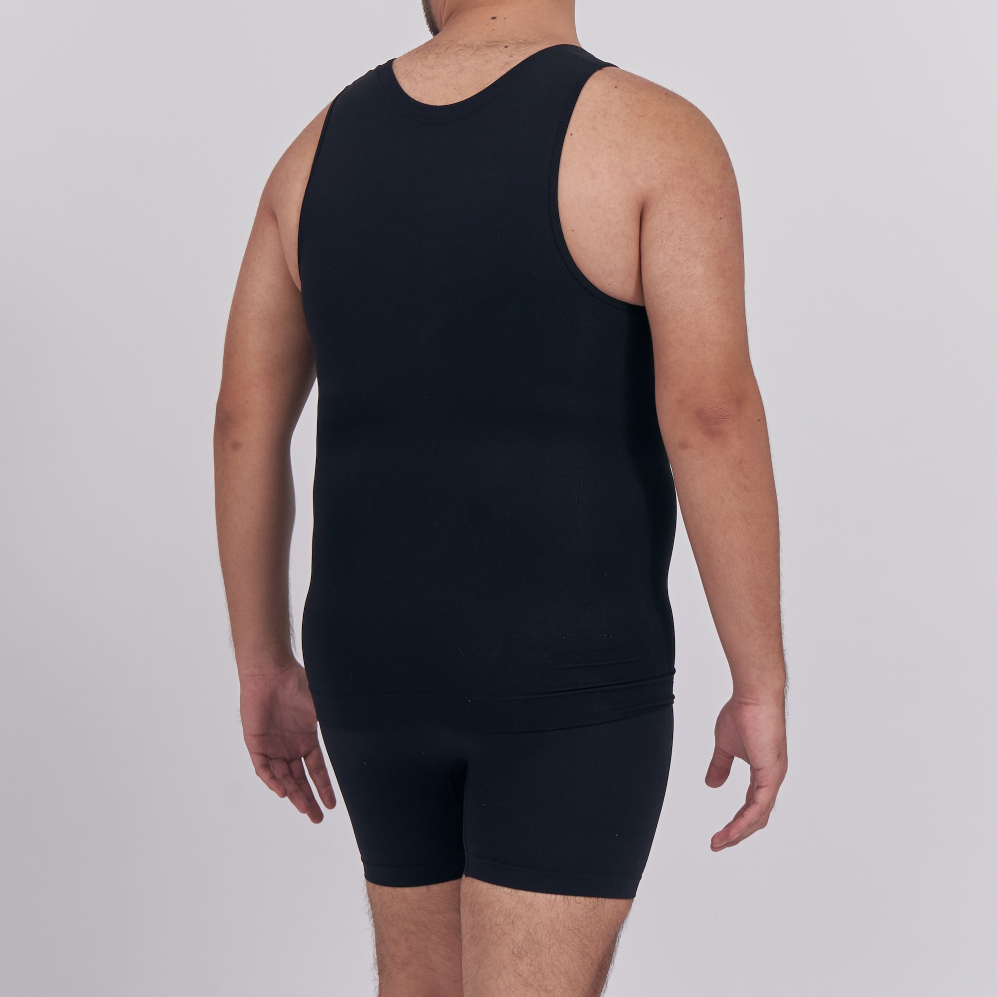 Person wearing a black tank top and shorts on a plain background