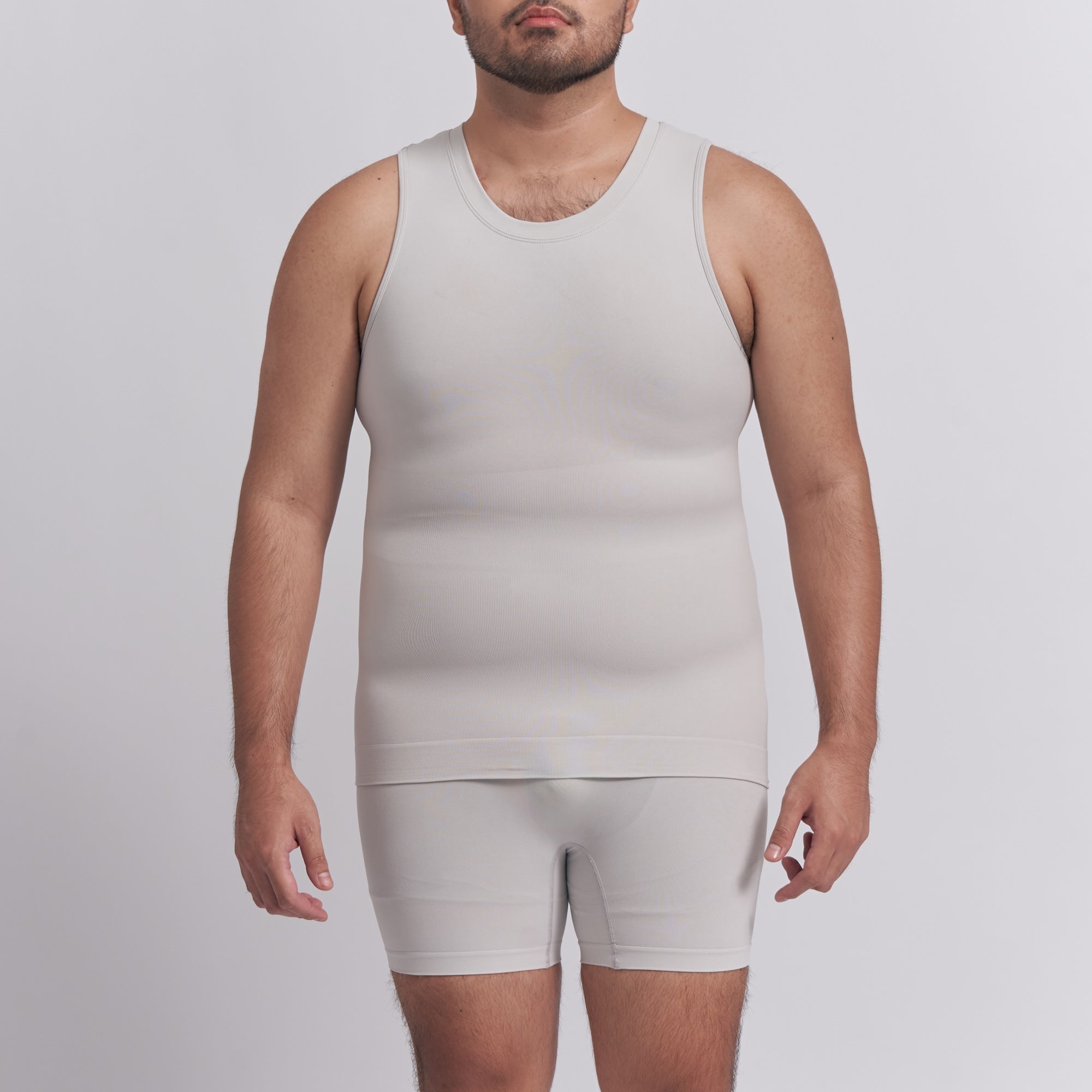 Man wearing a beige tank top and shorts set on a plain background