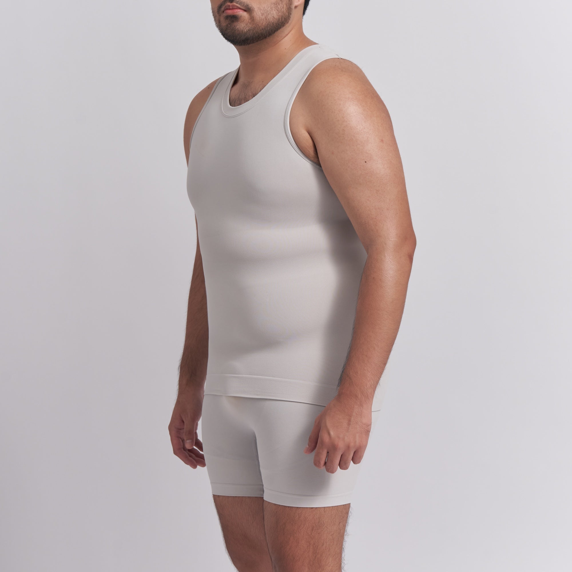 Man wearing a beige tank top and shorts set on a light gray background