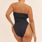 Black strapless swimsuit with high cut design on a beige background