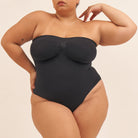 Person wearing a black strapless swimsuit against a beige background