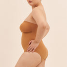Person wearing a strapless brown bodysuit against a beige background