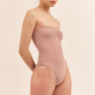 Woman wearing a strapless bodysuit against a beige background