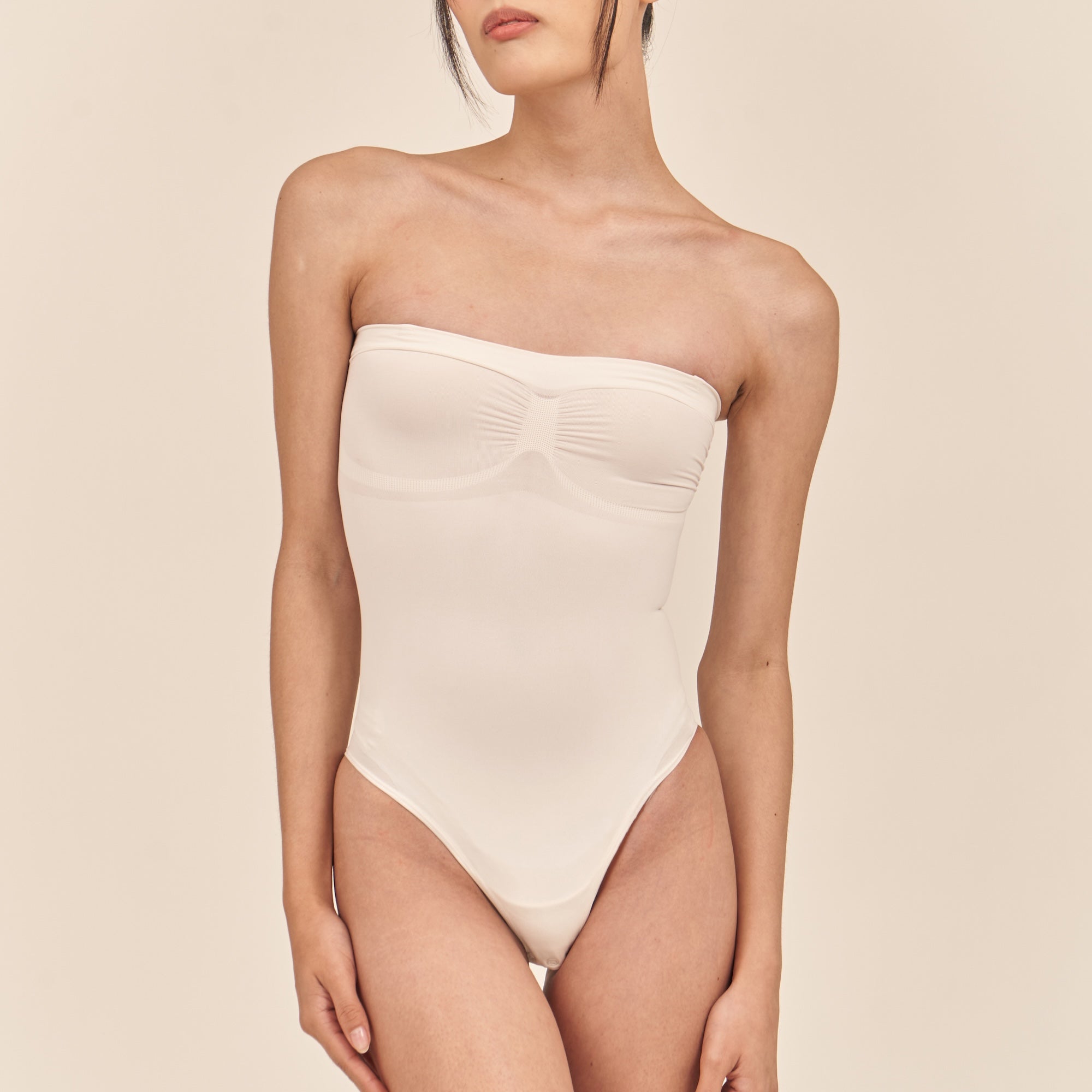 White strapless swimsuit worn by a model on a beige background