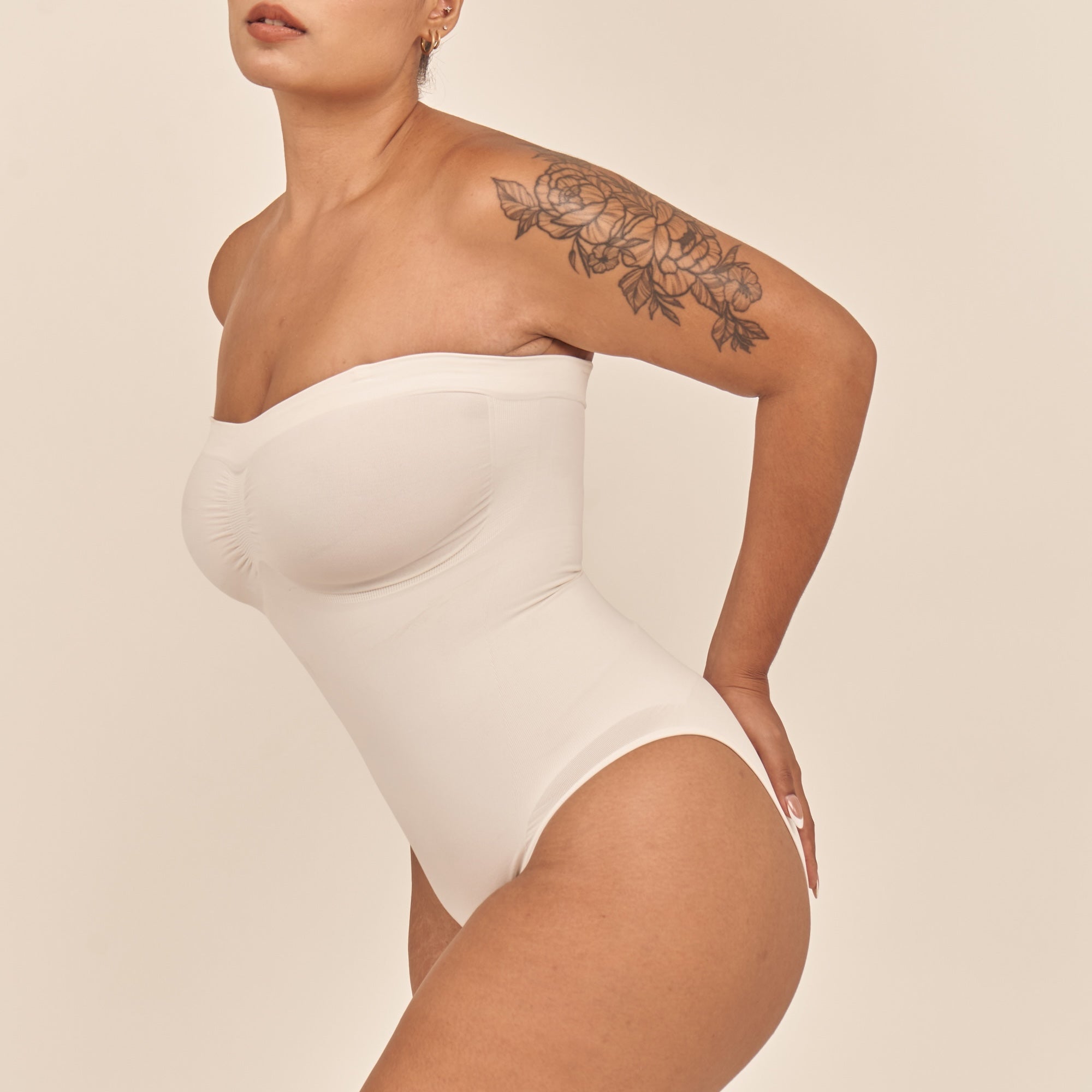 Woman wearing a white strapless bodysuit against a beige background