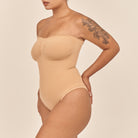 Woman wearing a beige strapless bodysuit against a plain background